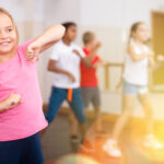 Positive girl exercising in group of classmates during dance class at school
